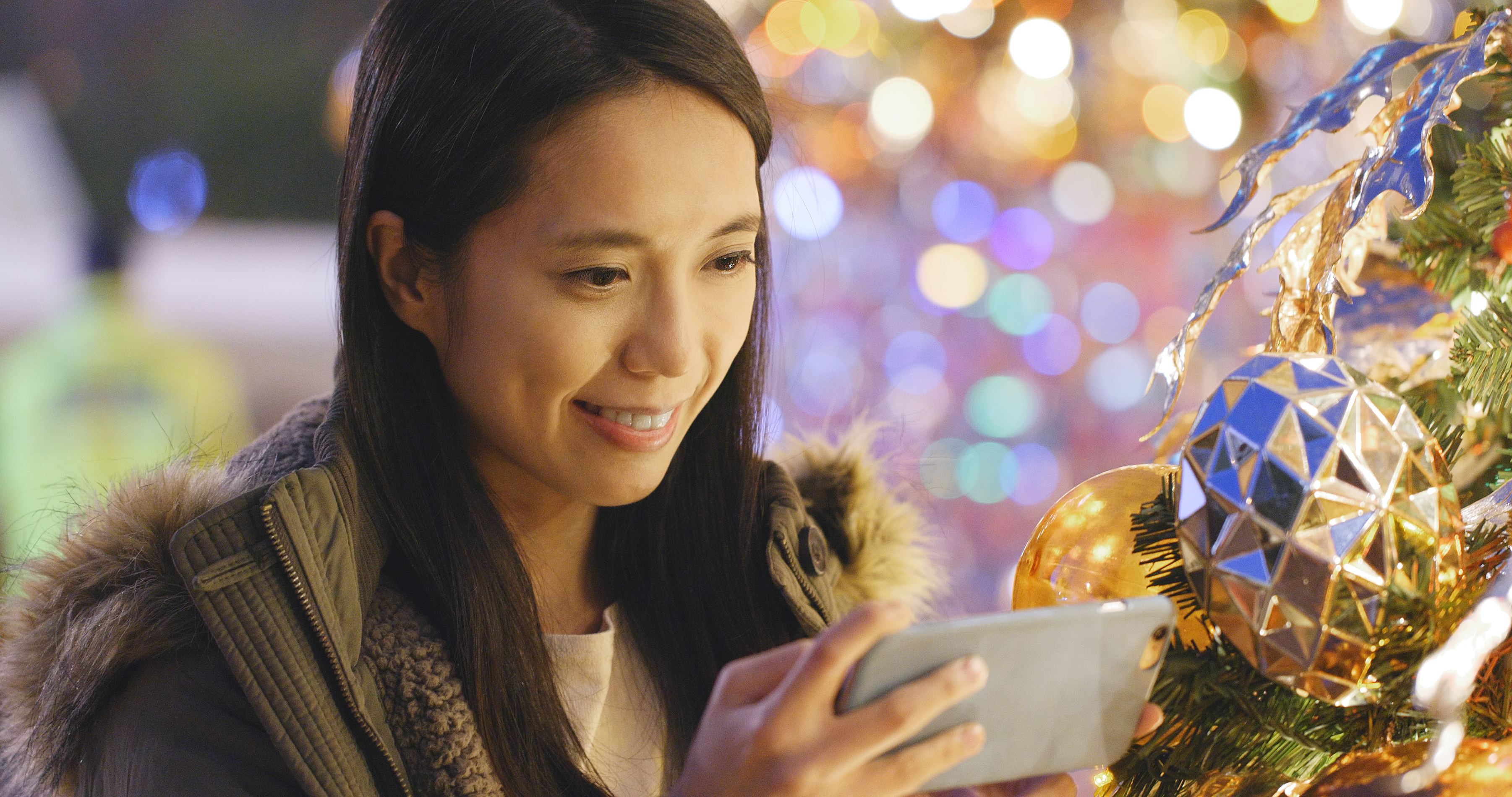 Woman taking photo on cellphone with Christmas tree decoration