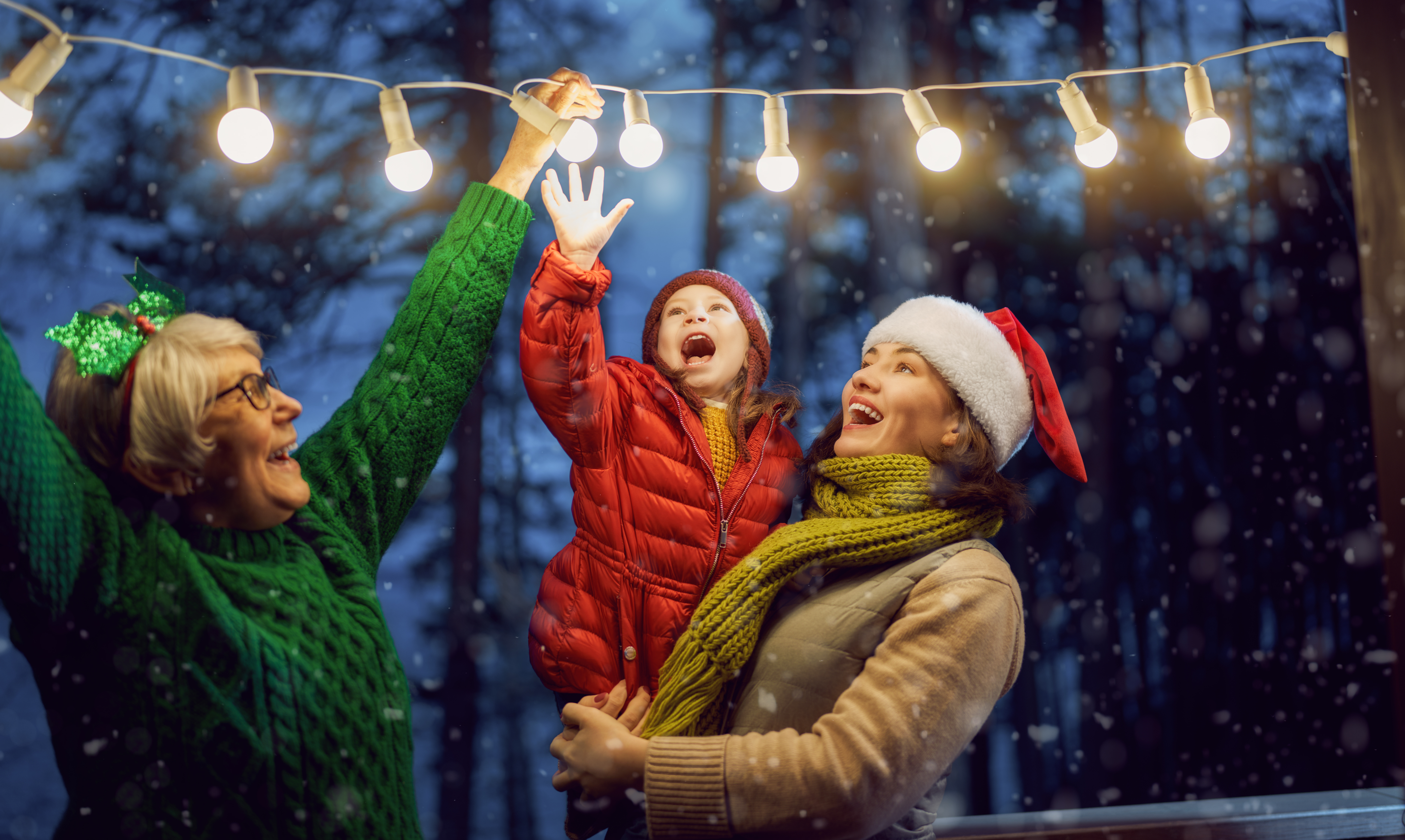 Merry Christmas and Happy Holidays! Cheerful mom, granny and cute girl decorating home. Parents and little child having fun outdoors. Loving family with garlands outside.