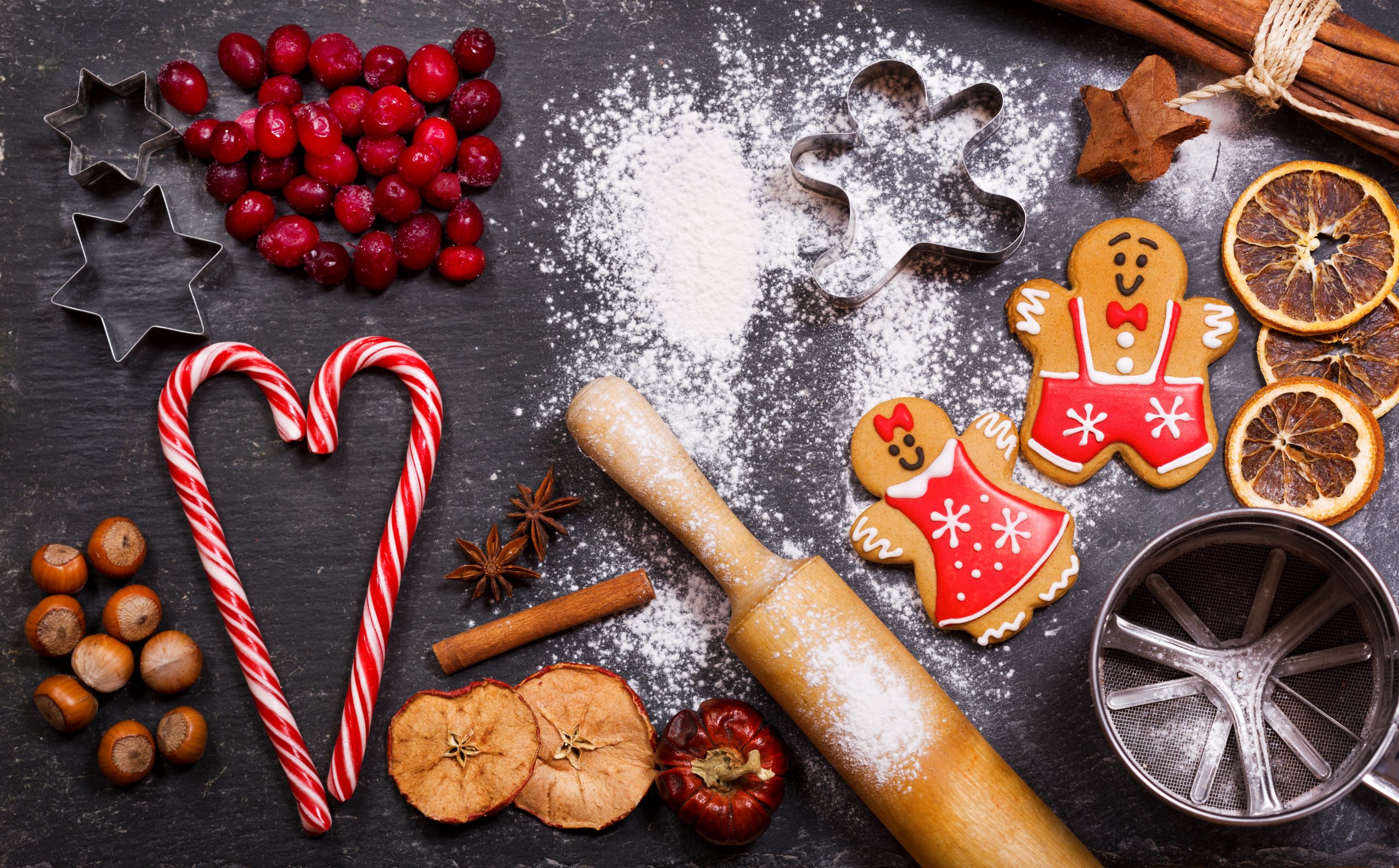 Christmas food. Homemade gingerbread cookies with ingredients for christmas baking and kitchen utensils on dark table, top view