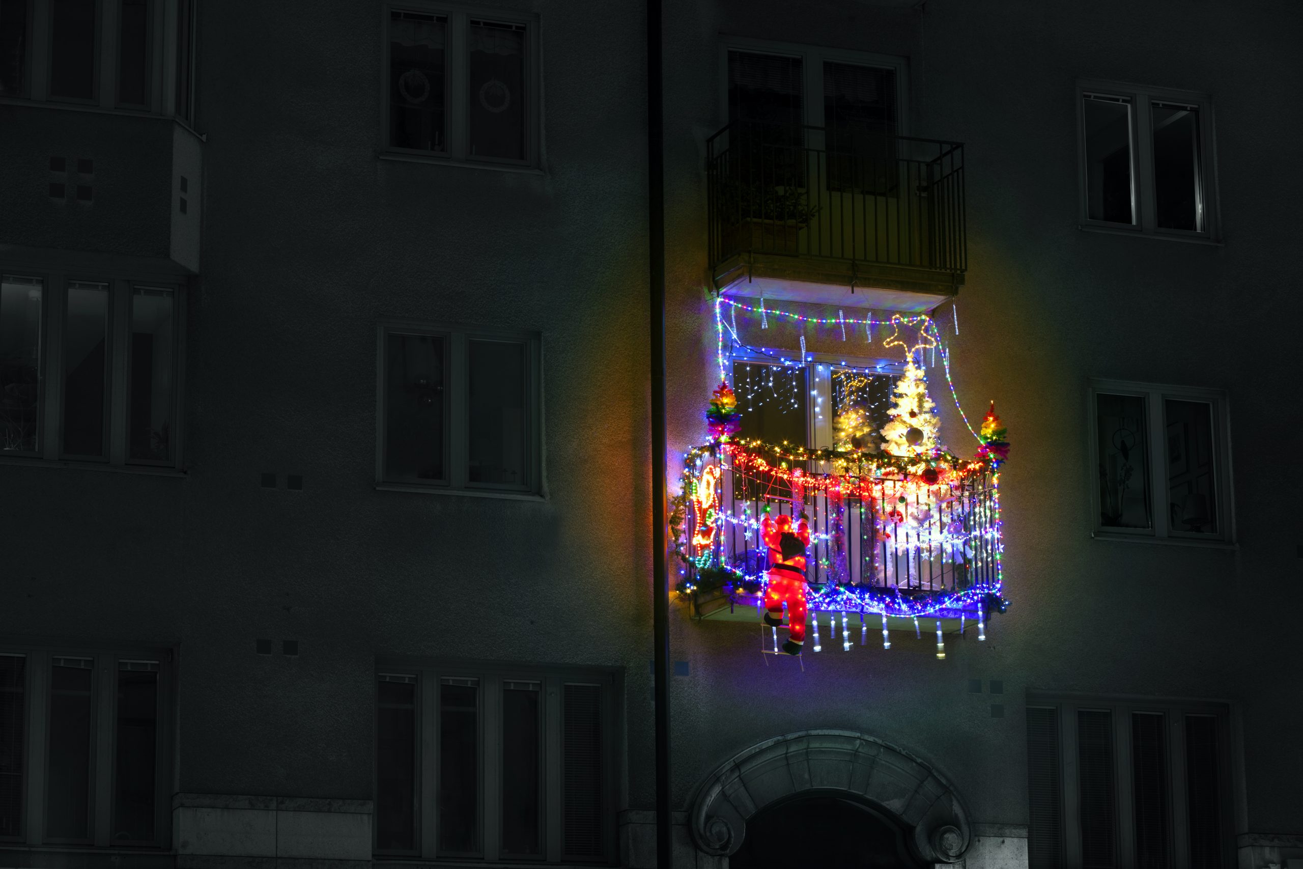 red jingle bells, lights, fir branches with ornaments on balcony in european city street
