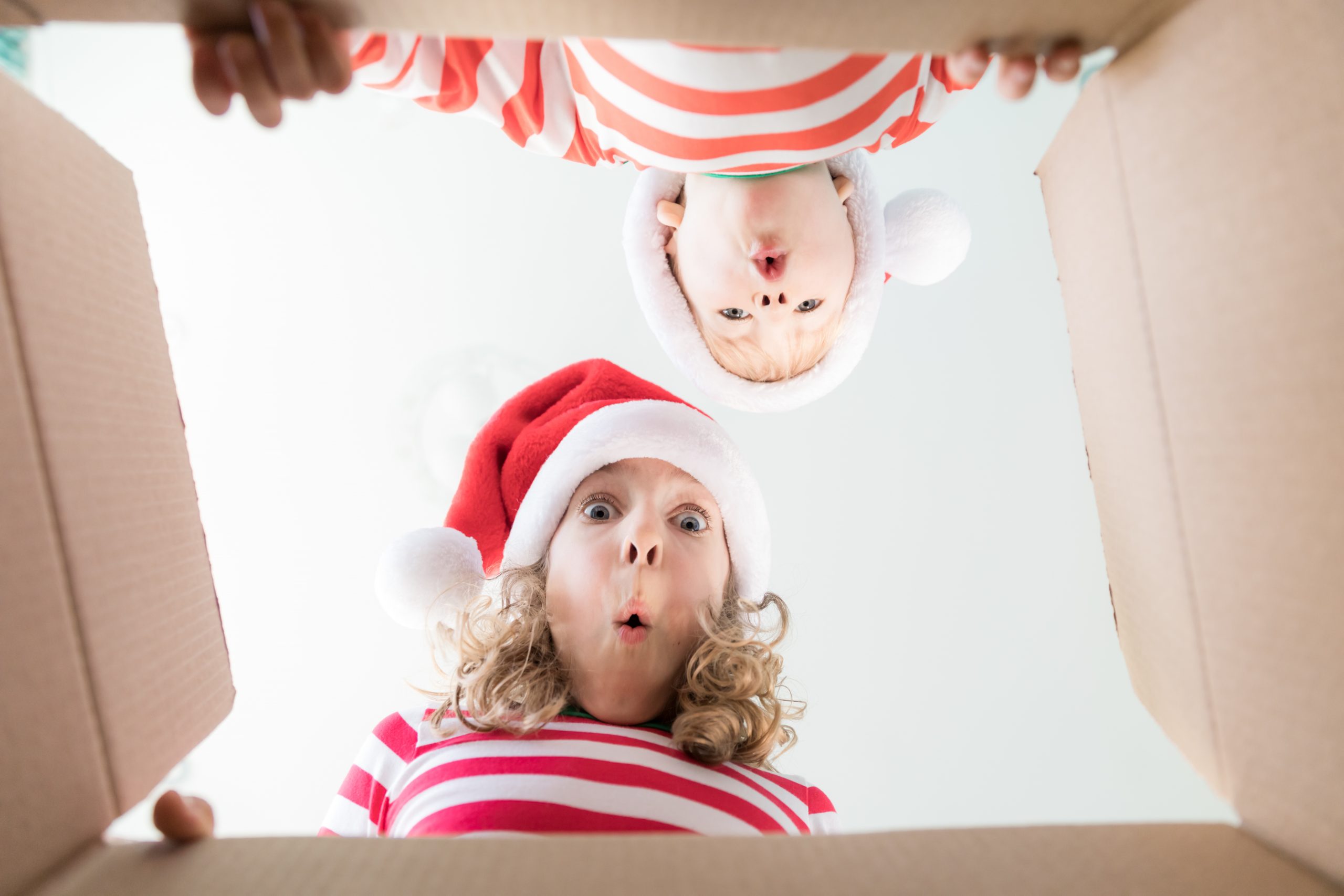 Happy children looking into the box. Funny surprised kids unpack Christmas gift box. Xmas holiday concept. Low angle view.