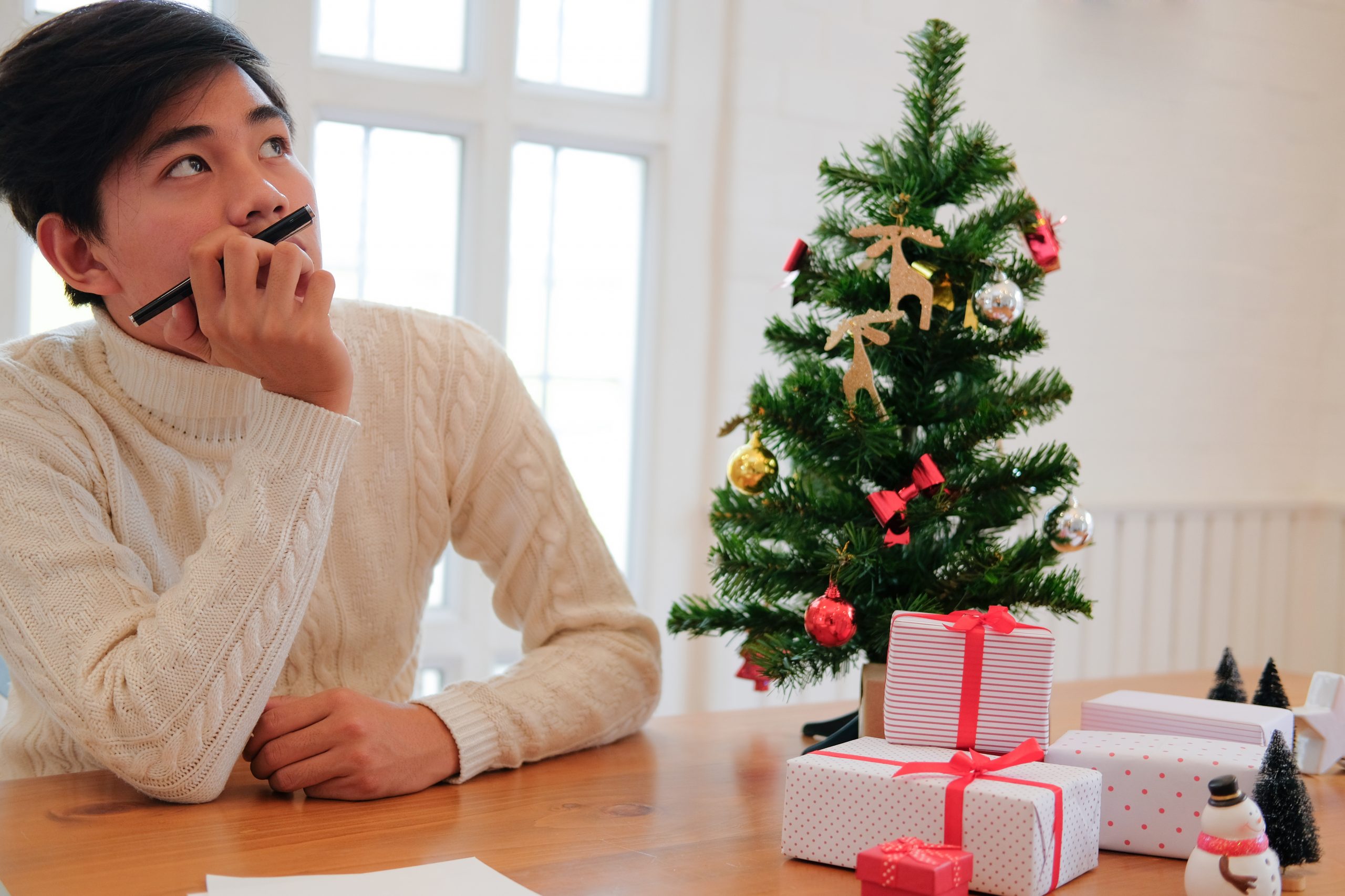 man wearing cream sweater thinking with pensive expression. christmas decoration at xmas new year holiday celebration.