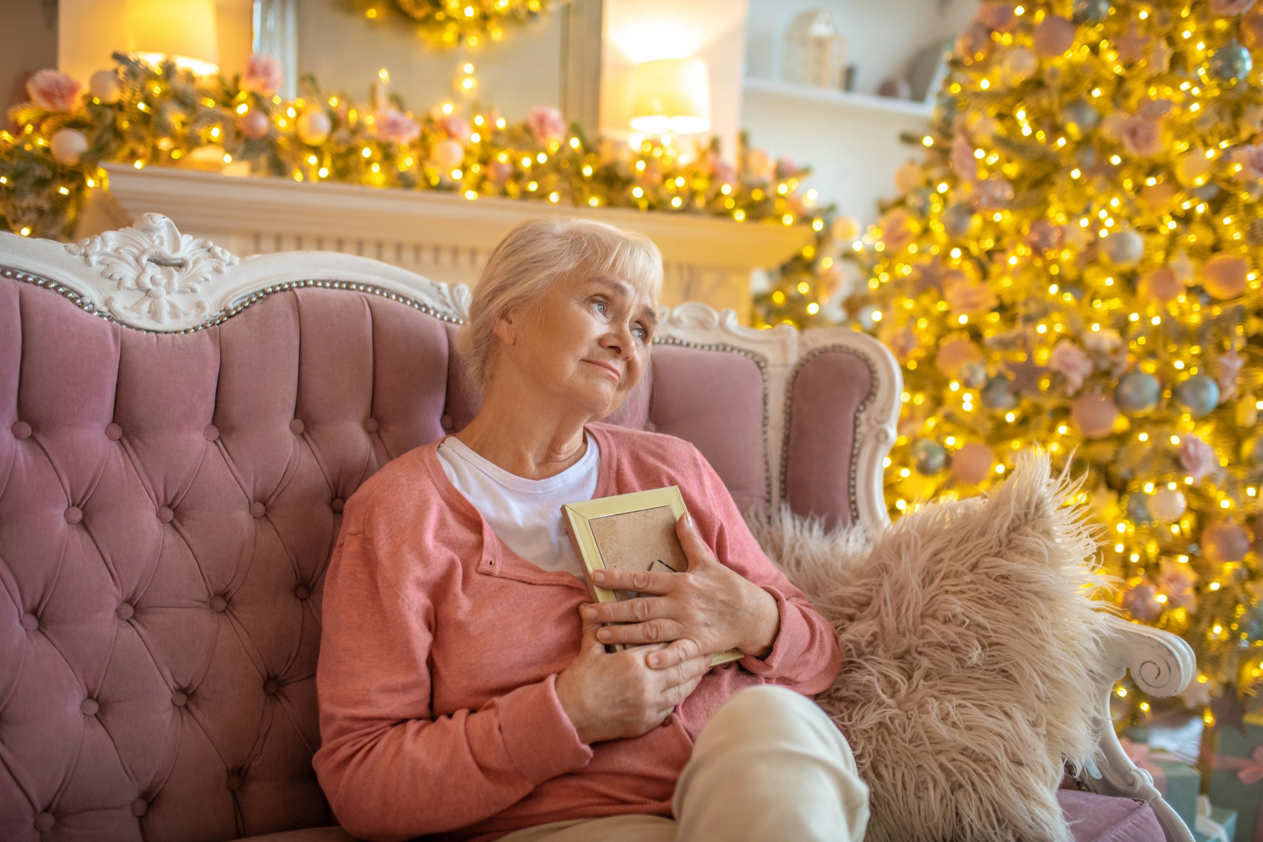 Lonely. Senior woman sitting on a sofa with a photo in her hand and feeling lonely